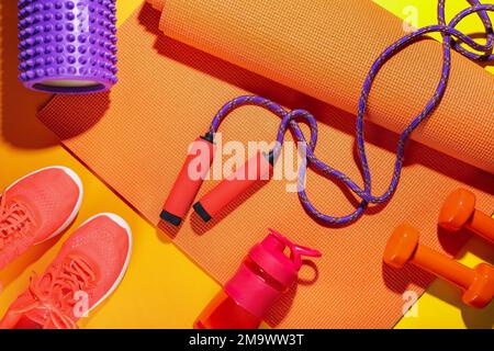 Corda da salto con tappetino, manubri, bottiglia e sneakers su sfondo colorato Foto Stock