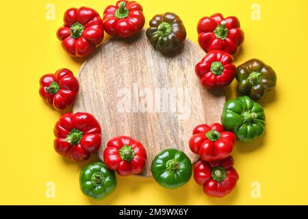 Composizione con peperoni freschi e piatto di legno su fondo giallo Foto Stock