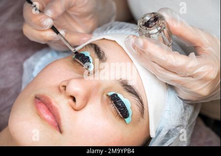 Primo piano ritratto di una donna su procedura di laminazione ciglia. Il maestro applica la tinta alle ciglia. Foto Stock