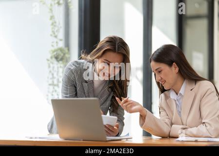 I giovani colleghi discutono i grafici dei prezzi aziendali e analitici utilizzando calcolatrici e laptop per calcolare dati finanziari, fiscali, contabili, statistici e. Foto Stock