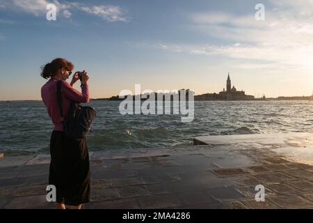 Una donna che fotografa il tramonto a Venezia Foto Stock