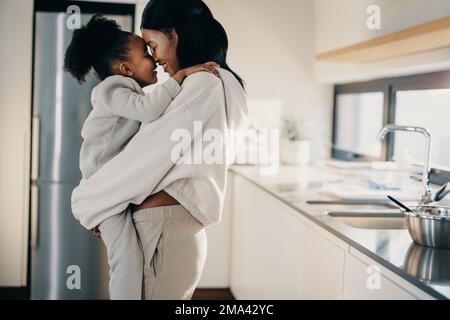 Madre amorevole e relazione figlia, donna che porta sua figlia. Mamma e figlia sorridono mentre si abbracciano in abiti corrispondenti a casa. Foto Stock