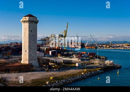 Faro, gru che scaricano navi portacontainer al porto container di Livorno, uno dei più grandi porti marittimi del Mediterraneo, in lontananza. Foto Stock