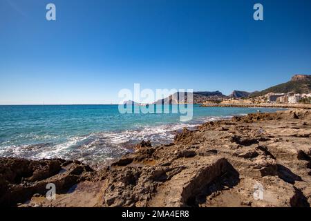Vista panoramica della zona rocciosa di Calpe con le onde del Mar Mediterraneo che si infrangono sulle sue pietre sotto un bel cielo azzurro soleggiato in autunno Foto Stock