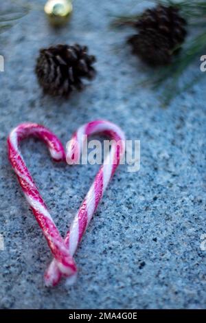 Cuore caramella con bastoni di Natale con lo sfondo sfocato di ananas e le loro foglie su una pietra in una giornata d'inverno. Foto Stock