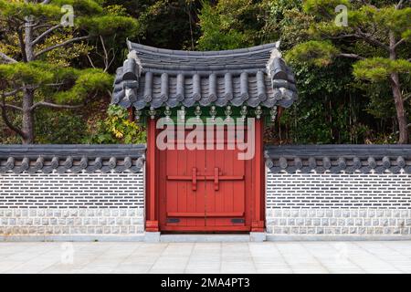 Cancello di legno rosso sotto il tetto piastrellato. Architettura orientale tradizionale nel parco pubblico di Busan, Corea del Sud Foto Stock
