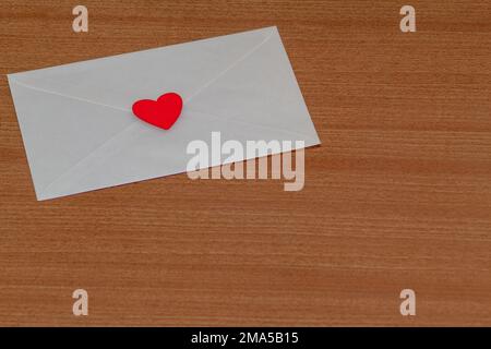 Lettera d'amore per San Valentino all'interno di una busta bianca chiusa e sigillata con un cuore rosso su uno sfondo di legno da un amante. Foto Stock