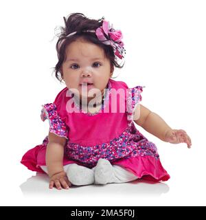 Carino, felice e ritratto di una bambina seduta isolata su uno sfondo bianco in uno studio. Girly, giocoso e innocente, adorabile e bambino piccolo Foto Stock