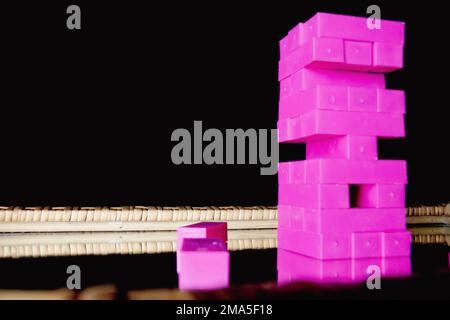 Il gioco per bambini in jenga di plastica rosa è iniziato come regalo di compleanno su uno specchio di legno. Foto Stock