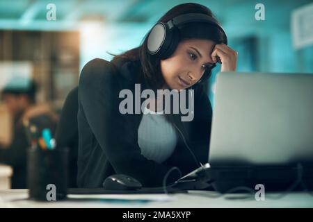 Cuori sulle ginocchia, cant ne ha senso. una giovane donna esausta che usa una cuffia in un ufficio moderno. Foto Stock