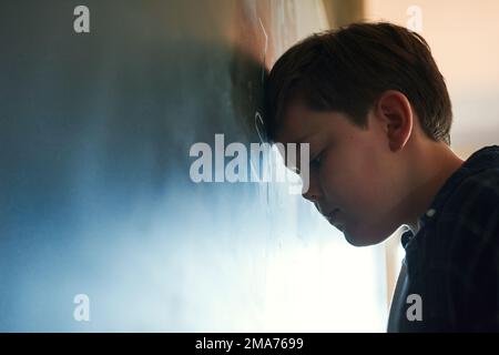 Tutti mi rideranno. un giovane ragazzo in piedi e si sente depresso mentre cerca di rispondere a una domanda sulla lavagna a scuola. Foto Stock