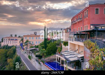 Taormina, Sicilia, Italia. Immagine del paesaggio urbano della pittoresca città di Taormina, Sicilia con il vulcano Mt. Etna sullo sfondo al tramonto. Foto Stock