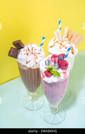 Bevande rinfrescanti estive, frullati, frullati pazzi con gelato, frutti di bosco, vaniglia, cioccolato. Su uno sfondo giallo blu brillante Foto Stock