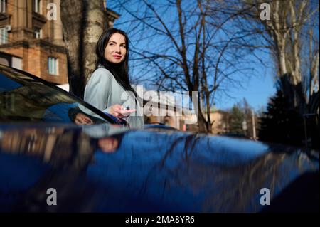 Bella donna d'affari caucasica fiduciosa uscire dalla sua auto moderna e metterla in allarme in ambiente urbano Foto Stock