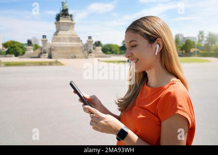 Vista laterale di una giovane donna ridente che sceglie la playlist guardando il suo smartphone nel parco cittadino di Sao Paulo, Brasile Foto Stock