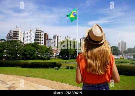 Ragazza brasiliana guardando la bandiera nazionale con San Paolo paesaggio urbano sullo sfondo, Brasile Foto Stock