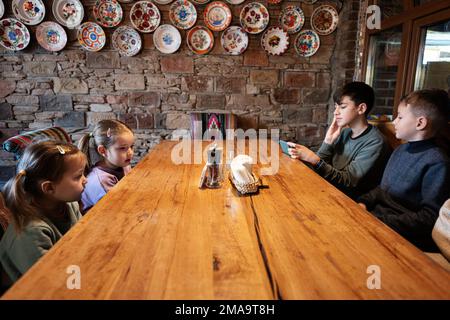 Quattro bambini si siedono in autentico ristorante ucraino, guardando sui telefoni. Foto Stock