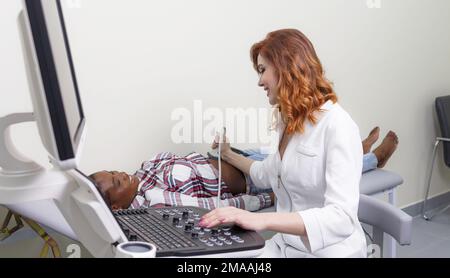 Procedura ecografica. La ragazza medico conduce un esame ecografico della cavità addominale di un paziente afroamericano. Foto Stock