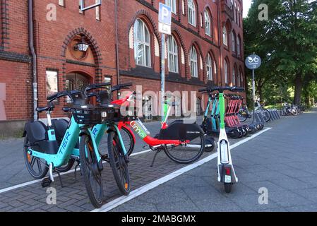 03.06.2022, Germania, , Berlino - e-scooters di voi, Tier e Lime società e biciclette elettroniche di Lime e Tier società in piedi su un marciapiede in un parki Foto Stock