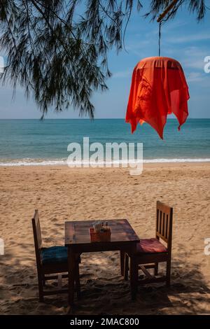 Tavolo da ristorante in legno e due sedie su una spiaggia tropicale con una lanterna rossa a Ko Lanta, Krabi, Thailandia Foto Stock