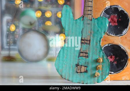 Grungy cartone modello di chitarra e cassa, sintetizzatore e drum kit sfocato in background, fare musica, performance, concetto di strumenti Foto Stock