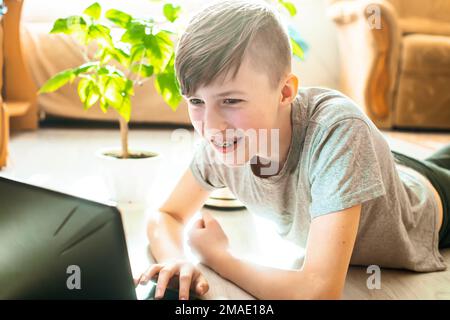 teenager in bretes on teeth programmi seduti al computer portatile sul pavimento. ragazzo in interni alla moda vicino a piante verdi alla moda da giardino d'inverno insegna lesso Foto Stock