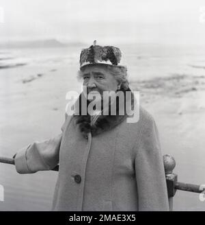 1950s, storica, una donna anziana elegantemente vestita che indossa un cappotto di cashmere, cashmere con colletto in pelliccia, sciarpa da collo e un cappello decorato in piuma che si trova sulla costa per la sua foto, Inghilterra, Regno Unito. Foto Stock