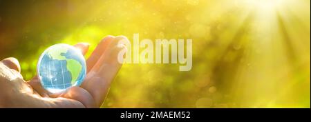La mano tiene lo strato di cristallo sotto forma di globo. Concetto e tema della natura, protezione ambientale. salvare la terra o il pianeta. Giornata della Terra Foto Stock