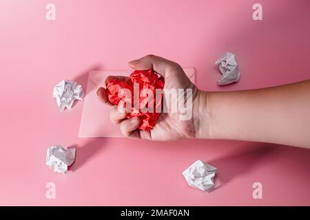 mano di un uomo aggressivo e frustrato che strinse il cuore dalla carta stropicciata. busta con frammenti di carta sparsi. Lettera a una persona cara su Valentin Foto Stock