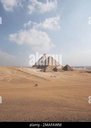 Vista delle piramidi di Giza, il Cairo, Egitto con cammelli a piedi in primo piano e la città sullo sfondo. Foto Stock