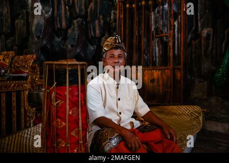 Bali - Indonesia - 10.22.2015: Anziano musicista indonesiano vestito con abiti tradizionali seduto da solo con una faccia diritta Foto Stock