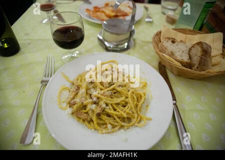 Piatto di spaghetti alla carbonara servito con vino rosso e pane in un tradizionale ristorante italiano. Foto Stock