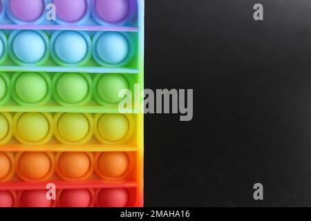 Multi-colorato anti-stress giocattolo quadrato e spinner popit semplice concavità su uno sfondo nero con spazio per il testo e con copyspace. Foto Stock