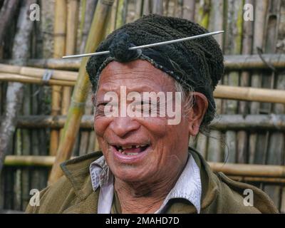 Ziro, Arunachal Pradesh, India - 02 19 2013 : Ritratto di felice vecchio Apatani tribale uomo con tradizionale pancia anteriore capelli e ago indossare cappuccio nero Foto Stock