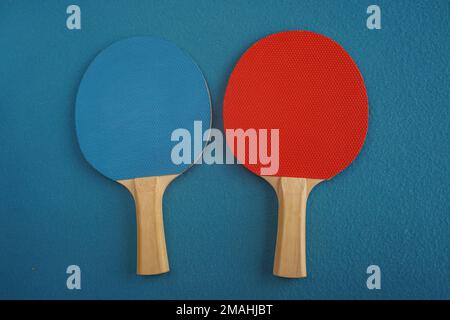 Le racchette da ping pong o da ping pong rosse e blu si trovano su uno sfondo blu con una vista ravvicinata dall'alto Foto Stock