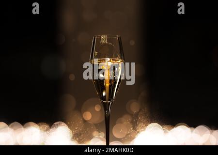 Bicchiere di champagne con bollicine su fondo scuro con bokeh. Celebrazione e concetto di festa. Foto Stock