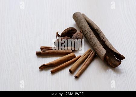 Cannella e noce moscata bastoncini di cannella spezie aromatiche su tagliere in legno con fondo bianco Foto Stock