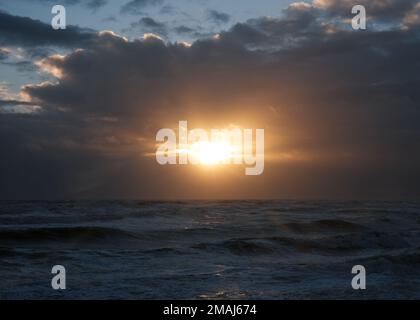 Sunburst attraverso le nuvole mentre si imposta sul canale di lingua inglese. - St Leonards on Sea, Regno Unito Foto Stock