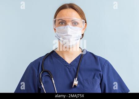 Medico in maschera medica con stetoscopio su sfondo blu Foto Stock
