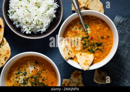 Zuppa di lenticchie rosse con latte di cocco e curry accompagnati da riso basmati e pane naan su sfondo blu scuro Foto Stock