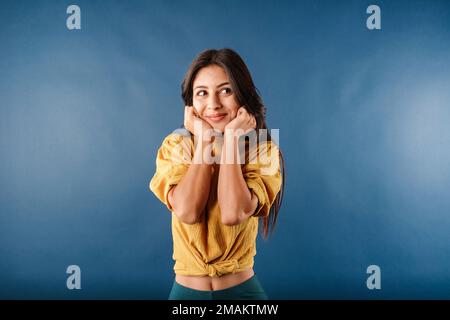 Ritratto di giovane donna brunetta isolato su mani di sfondo blu in pugni, toccando mento, guarda eccitatamente alla macchina fotografica ed è dumbfounded. Non posso Foto Stock