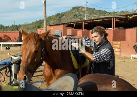 Ritratto di un cavaliere adulto sicuro regolazione sella di cavallo prima di cavalcare in country club Foto Stock