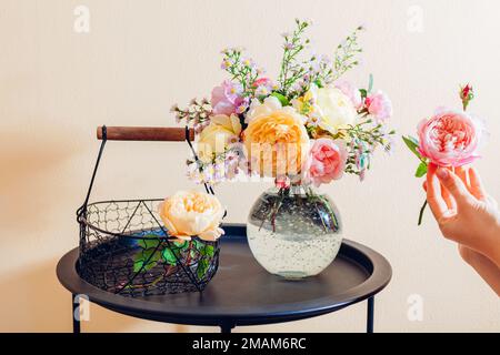 Primo piano di rose inglesi fresche. Donna fa bouquet in vaso trasparente di fiori rosa giallo arancio sul tavolo a casa. Foto Stock
