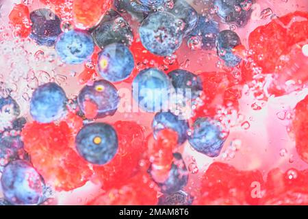 Acqua con bacche fresche, primo piano. Vista ravvicinata dei mirtilli e dei lamponi sullo sfondo dell'acqua. Consistenza di mirtilli e lamponi con m Foto Stock
