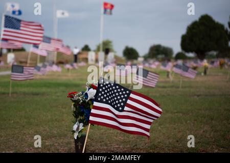 La bandiera americana sbatte nella brezza accanto a un vaso di fiori in cima a una lapide a Lawnhaven Memorial Gardens, San Angelo, Texas, 30 maggio 2022. Le bandiere sono state piantate da volontari della comunità di San Angelo e dallo staff di Lawnhaven presso la tomba di ogni membro del servizio in preparazione di una cerimonia del Memorial Day Foto Stock