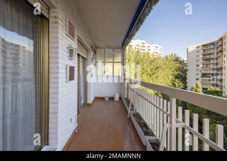 Terrazza all'aperto di una casa in un edificio residenziale con ringhiere dipinte di bianco, pavimenti marroni e vista su un giardino comunale con alberi Foto Stock