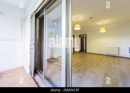 Soggiorno vuoto con pavimento in rovere con accesso alla terrazza e bianco, recinzione pieghevole e lampade a sospensione Foto Stock