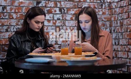 Due belle ragazze sono seduti in un caffè e parlare con i telefoni. Foto Stock