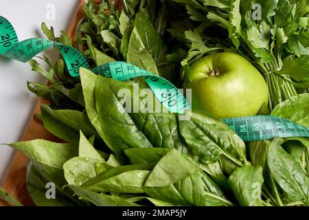 alcune verdure verdi e una mela su un tagliere con nastro di misurazione intorno a loro per mostrare come sono fatte Foto Stock