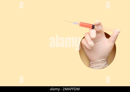 Medico di sesso femminile con siringa su sfondo beige Foto Stock